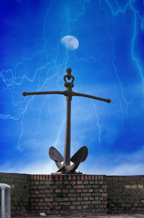 Anchor on a wall. Against a dramatic cloudscape with lightning and moon.の写真素材