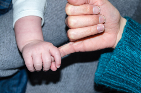 Small baby hand holds a finger of one hand adult.の写真素材