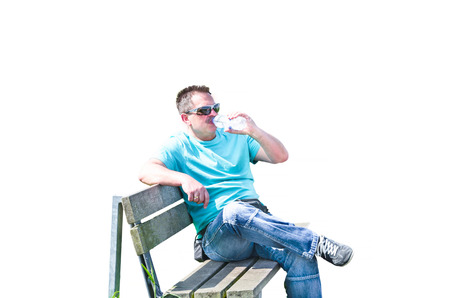 Man sitting on a bench drinking from a bottle of mineral water, isolated on white background.の写真素材