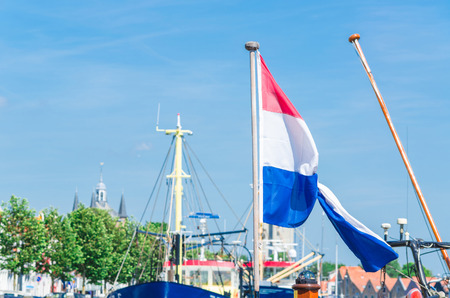 Looking in a dutch Marina, Mast with flag of the Netherlands against blue sky.の写真素材