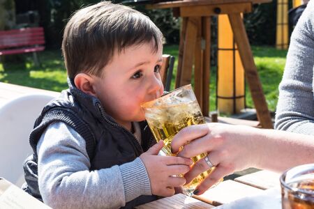 Child drinks juice from a glass in a garden restaurant.の写真素材