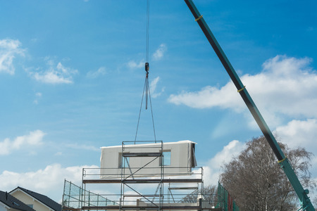 A wall part of a prefabricated house on a crane against blue sky.の写真素材