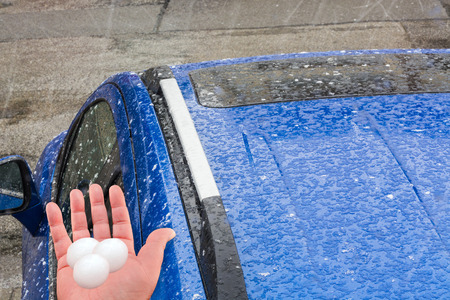Hail falls on a blue car roof.