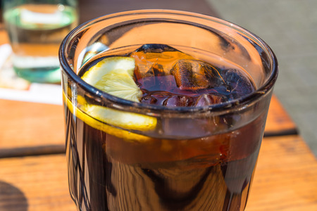 Detail, glass of cola with ice and lemon on a wooden table.