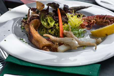 Closeup of various grilled kinds of fish on a white plate in the restaurant.