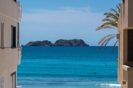 Overlooking the blue sea in the foreground a Spanish style house and a palm tree.の写真素材