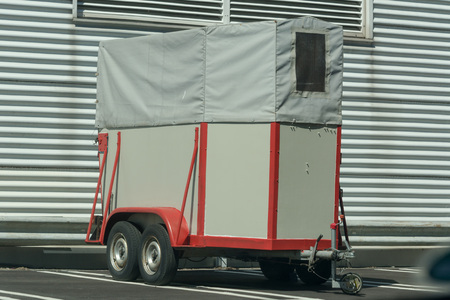 Old horse transport trailer in front of a metal wall.