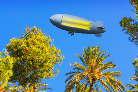 Landscape, tree tops of pines and palm trees on the Mediterranean Sea on Mallorca in Spain. In the sky a zeppelin with banner, copy space.の写真素材