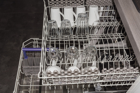 View from above on an open dishwasher with clean cup, glasses and plates.