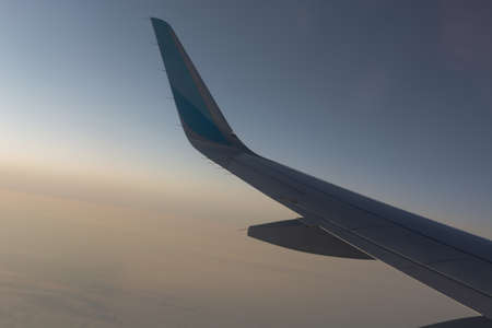 In the air, view of the airplane wing with horizon of dark blue sky and clouds background in sunrise...