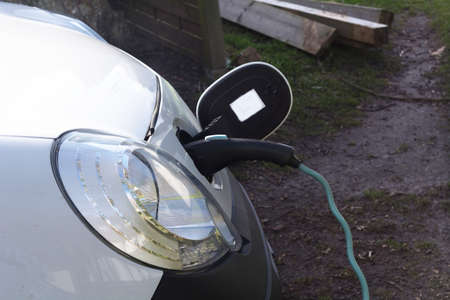 EV car or electric vehicle at the charging station with the power cord adapter plugged into blurred...