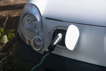 EV car or electric vehicle at the charging station with the power cord adapter plugged into blurred...