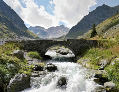 A small bridge over a roaring mountain stream. An impressive mountain backdrop rises in the background.の写真素材