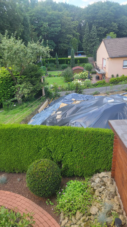 A construction site in a suburban neighborhood, featuring an excavated area covered with a tarp, a wooden shed, and residential houses in the background.の写真素材