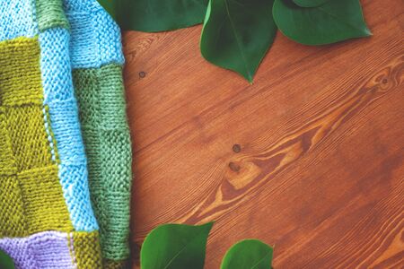 wooden background with lilac leaves and knitted scarf top view close-up