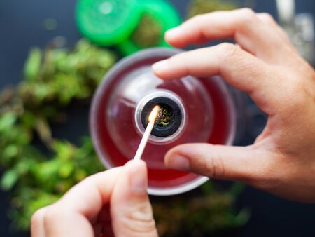 A girls hand sets fire to a match with a strong marijuana herb. smoking cannabis from a bottle and...