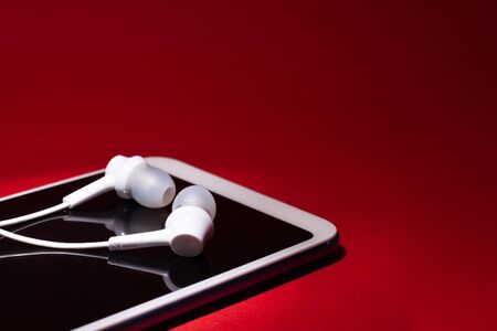 Concept: listen to music from the phone.smartphone with white headphones on a red background closeup. copy spaceの写真素材