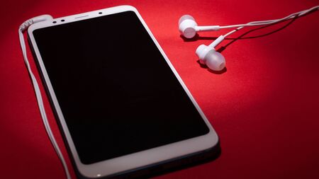Concept: listen to music from the phone.smartphone with white headphones on a red background close-up.の写真素材