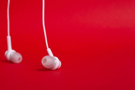 Concept: white headphones (earphones) on a red background with copy space close upの写真素材
