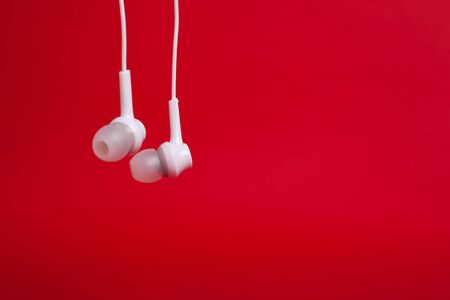 Hanging  white headphones (earphones) on a red background  with copyspace closeupの写真素材