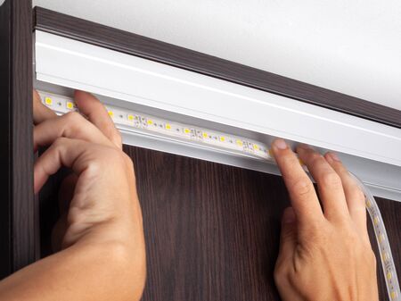 Electrician hands install LED strip lighting  in the niche of the cabinet to illuminate the wardrobe.の写真素材