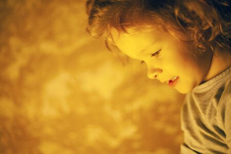 little girl in a dark room with a bright yellow lamp. out of focus.の写真素材