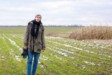 unshaven handsome young guy stands among spring green field.