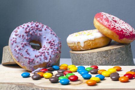 sweet colored donuts with icing and assorted candy on forest decorative wooden coasters on a gray background.の写真素材