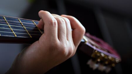 male hand holds a chord on an acoustic six string guitar close-up.