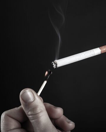 lighting a cigarette with a burning match in black and white.の写真素材