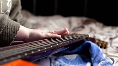 children's hand on the neck of an acoustic guitar orange color. learning to play the instrument.の写真素材