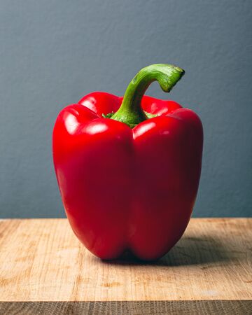 big red bell pepper on a wooden stand on a gray background.