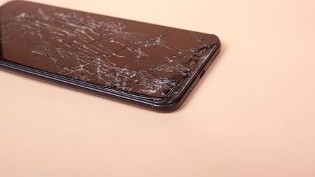 broken touchscreen black phone, smartphone, broken glass display smartphone on a beige background.