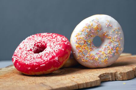 sweet multi-colored
 assorted donuts with icing and powder on a wooden board on gray background.の写真素材