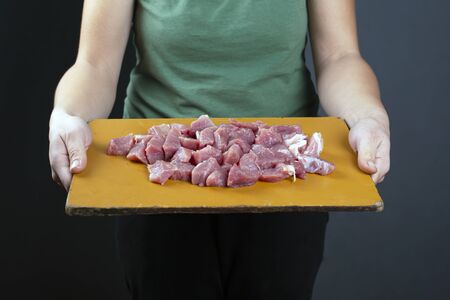 girl holding chopped meat on a wooden board preparation for cooking on a dark background.の写真素材