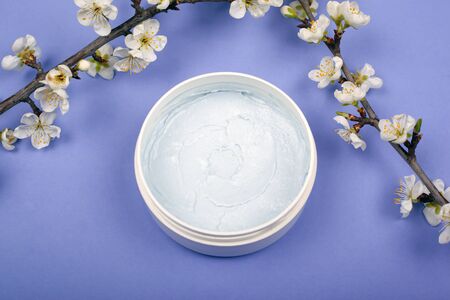 body scrub with branches of white cherry flowers on a violet background close-up, body care product.