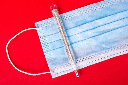 protective medical face mask and thermometer on a red background. protection against coronavirus...