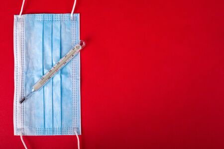 protective medical face mask and thermometer on a red background.with copy space. protection against...