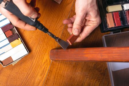 restoration of wooden furniture. master fixes a scratch on the table leg with a wax pencil and a...