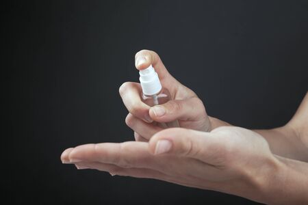 antibacterial spray applied on hands on a dark background close-up. antiseptic bottle, protection against viruses covid-19 and bacteriaの写真素材