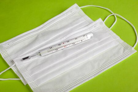 Thermometer and medical mask on a light green background close-up. defence from spread 2019-nCoV,...