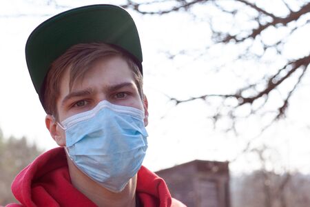guy dressed in red is standing in the street in a medical mask close-up, preventing the spread of the virus covid-19, health concept.の写真素材