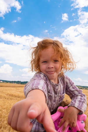 beautiful little girl sticks her finger into the camera against the background of blue sky and white clouds.の写真素材