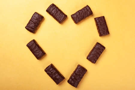 chocolate candies laid out in the shape of a heart on a yellow background top view.