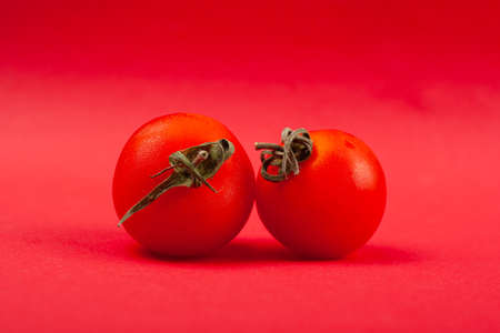 two small red tomatoes close-up on a red background.の写真素材