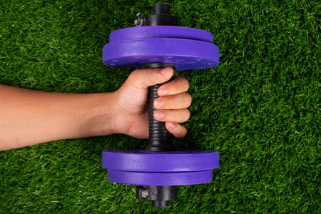 purple dumbbell in hand on green grass background close-up.の写真素材