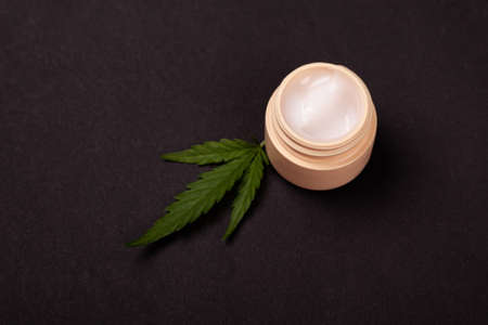 beauty, skin care cosmetics with marijuana extract. rejuvenating hand cream with medical cannabis plant leaf on black background.の写真素材