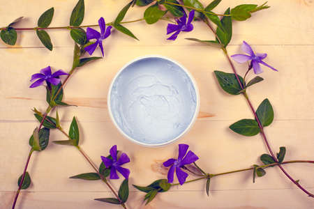 body cosmetics, beauty, scrub for skin care on a wooden background with branches of purple wildflowers, flat lay, top view.の写真素材