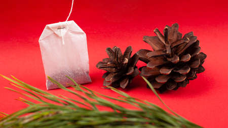 white paper tea bag with pine cones and spruce branches on a red background close-up, tea with forest aroma.の写真素材
