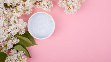 white body cosmetics on a pink background with branches of a white blooming lilac close-up copy space, skin care, beauty, scrub.の写真素材